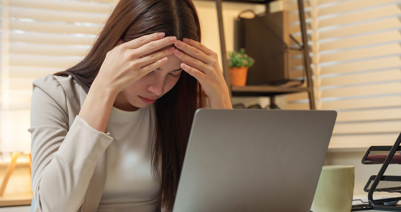 Asian-woman-holding-head-while-working-on-laptop
