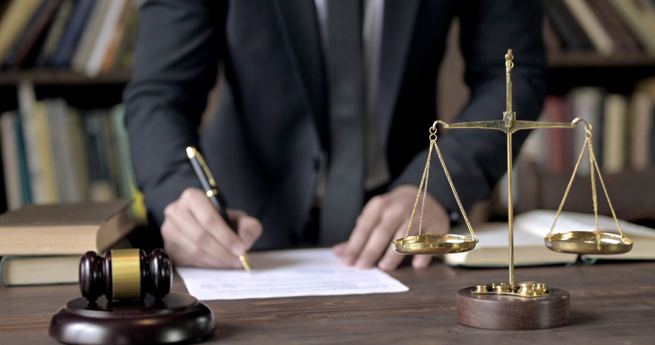 Close-up-of-lawyer’s-hand-writing-on-paper-beside-gavel
