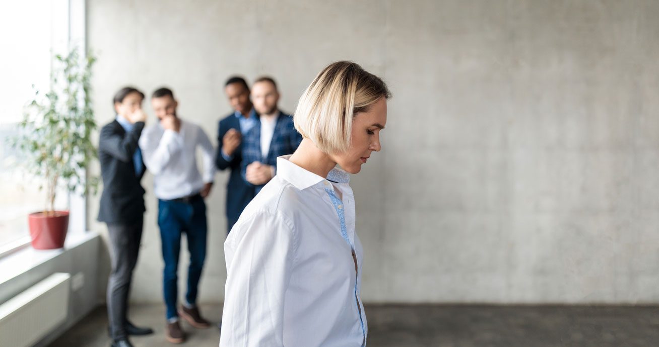 Male-colleagues-whispering-behind-woman-in-office