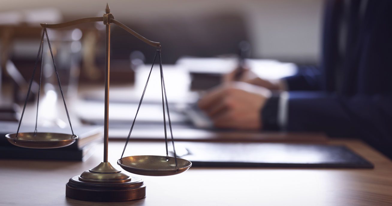 Scales-of-justice-in-foreground-with-blurred-lawyer-in-background