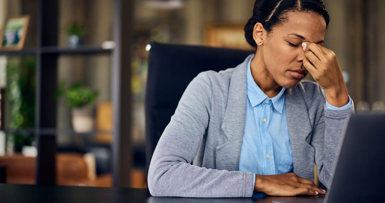 Woman-holding-head-while-sitting-at-desk-with-laptop