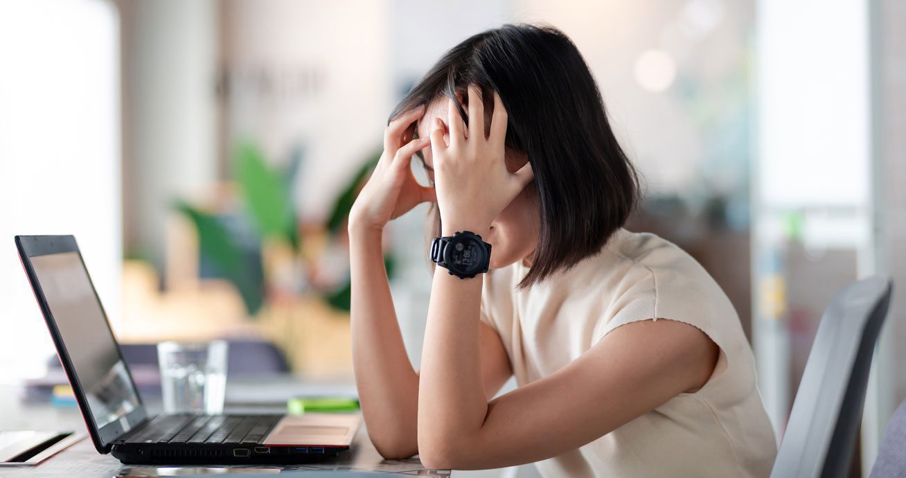 Woman-sitting-at-desk-using-laptop-with-hand-on-face