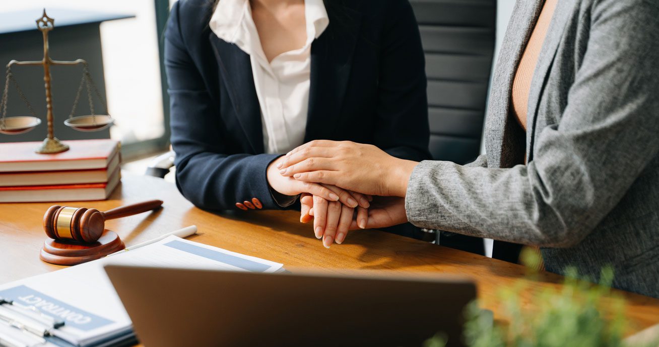 Close-up-of-two-people-holding-hands-over-contract-papers-on-desk