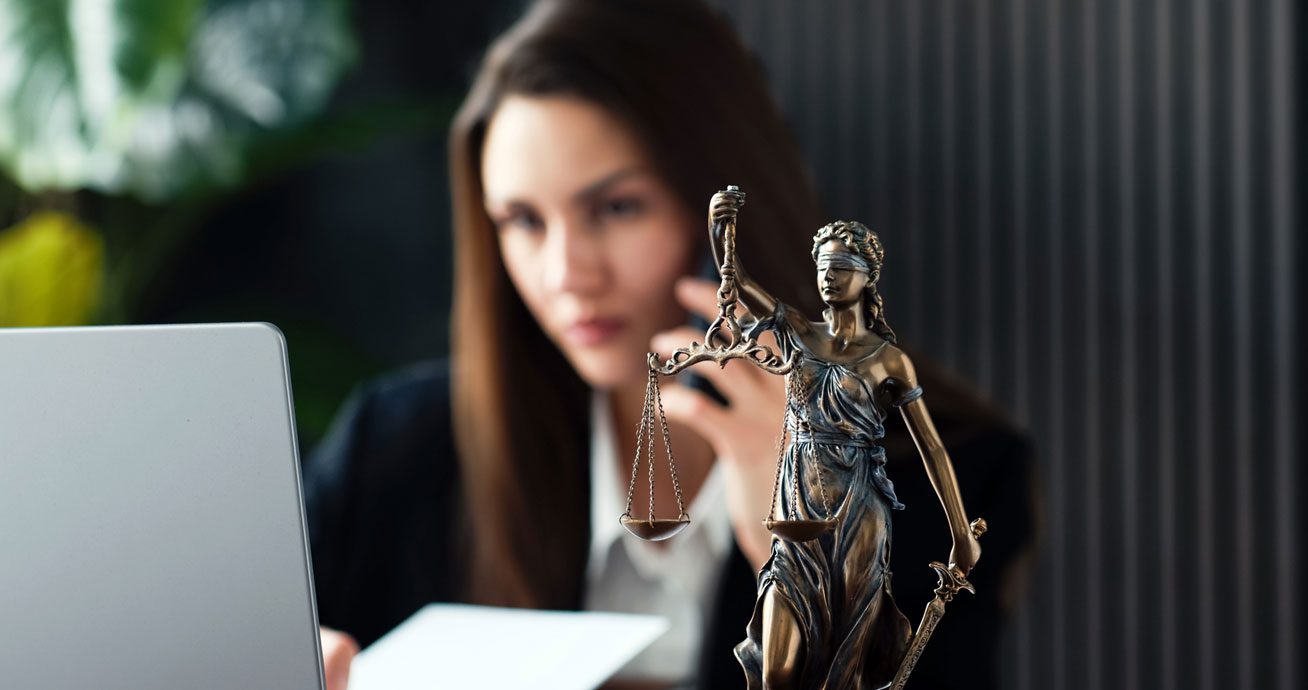 Female-lawyer-working-on-laptop-beside-Lady-Justice-statue