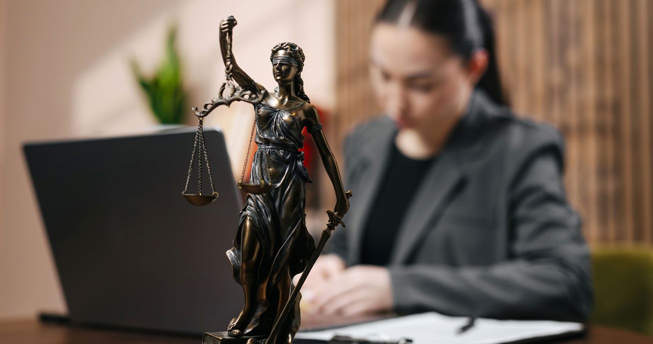 Professional-woman-sitting-at-desk-with-Lady-Justice-statue-nearby