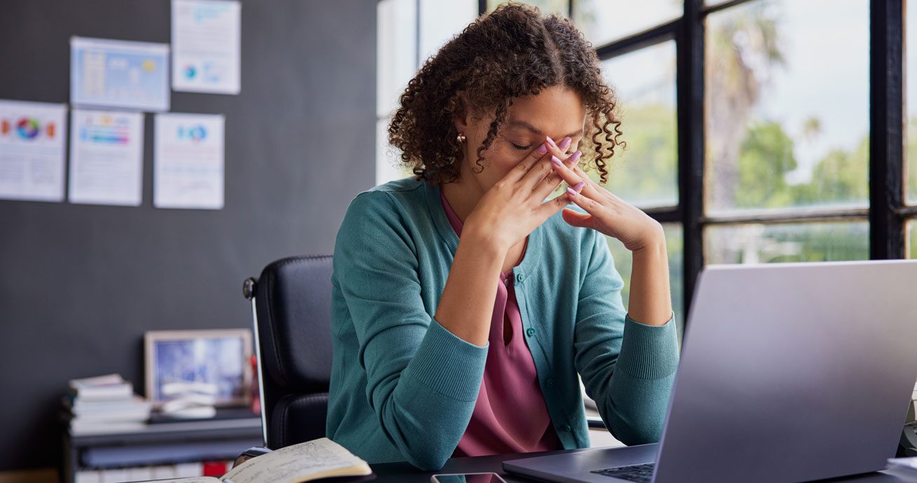 Woman-holding-head-while-working-at-laptop