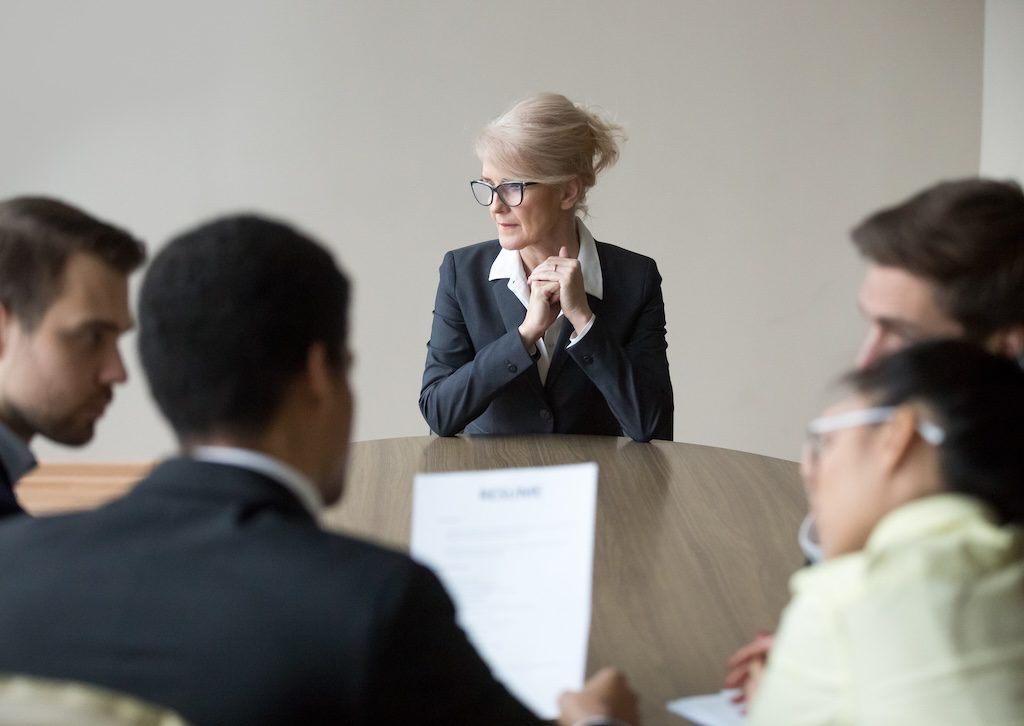 group-meeting-around-a-table-with-one-woman-standing-at-the-front