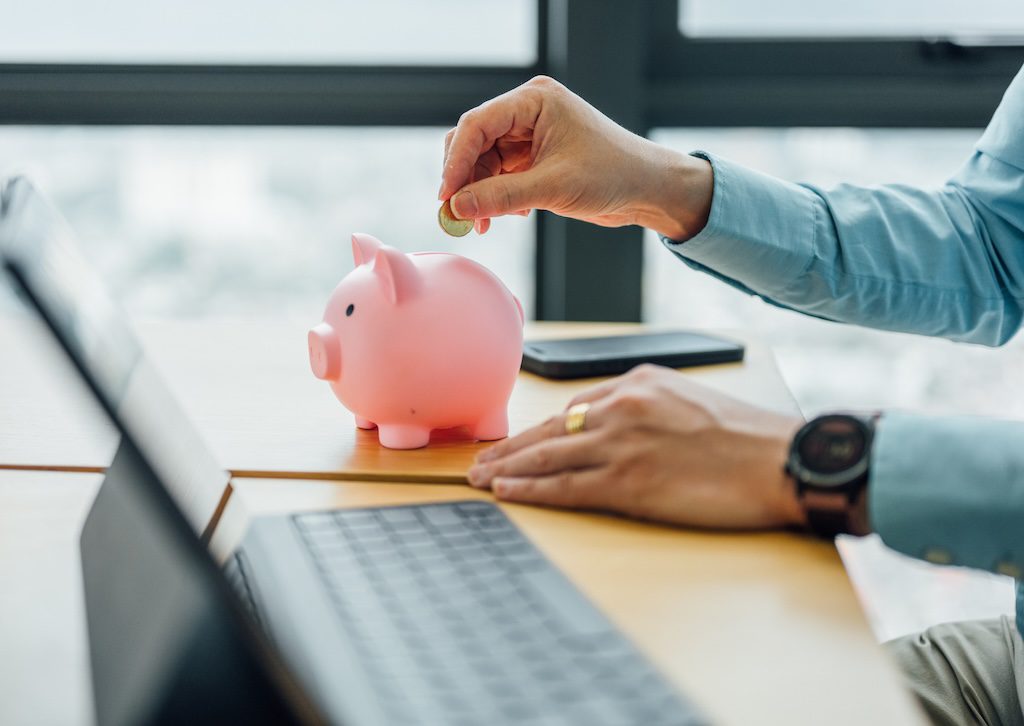 person-dropping-a-coin-into-a-pink-piggy-bank-on-a-desk
