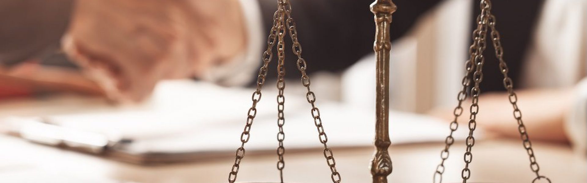 brass-scales-of-justice-on-a-desk-with-two-people-shaking-hands-behind