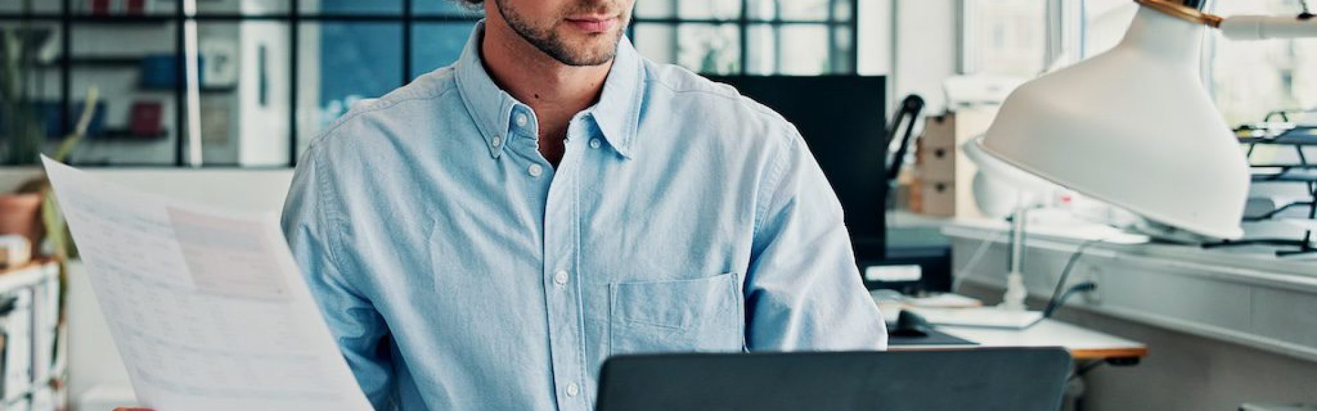 man-reviewing-a-document-at-a-desk-with-a-laptop-and-paperwork