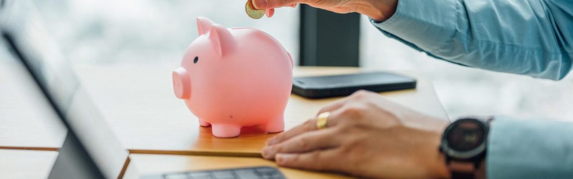 person-dropping-a-coin-into-a-pink-piggy-bank-on-a-desk